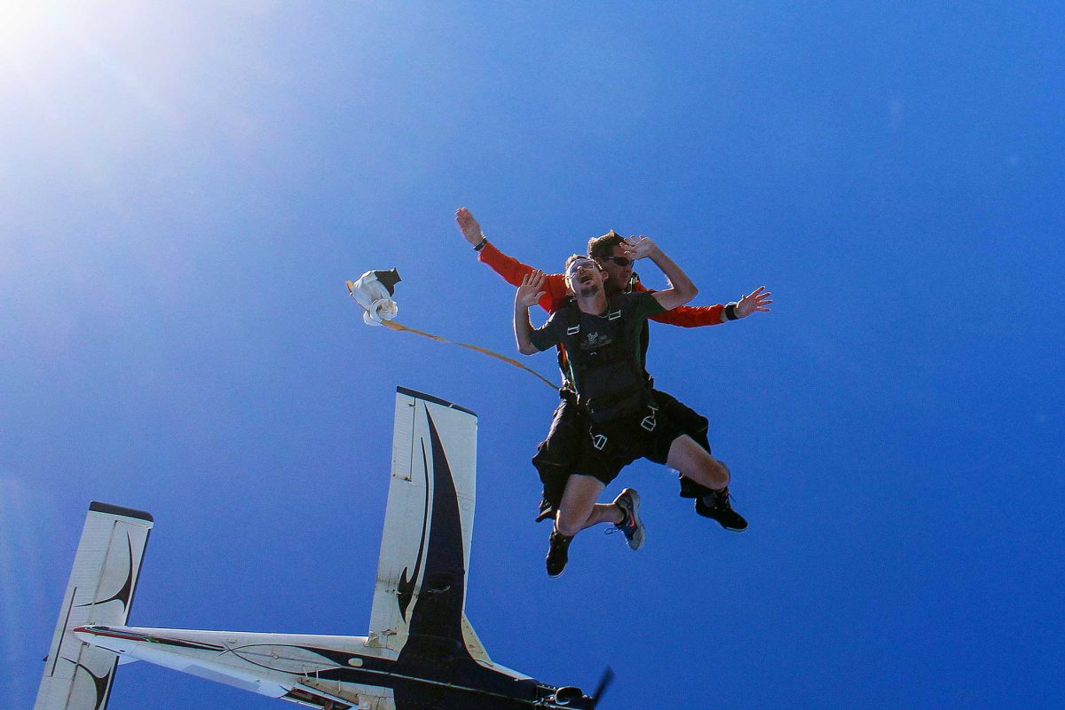 Instructor and student skydiving with black and white plane behind them.