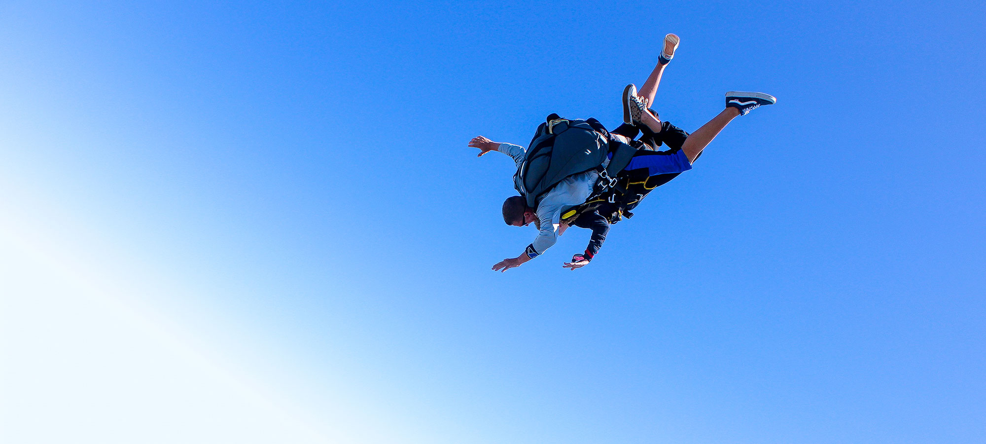Tandem instructor and student in free fall with bright blue sky in the background.