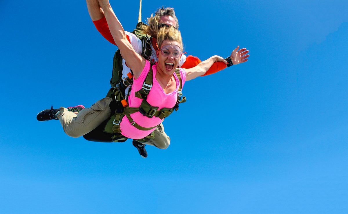 Women wearing pink shirt tandem skydiving with look of sheer excitement.